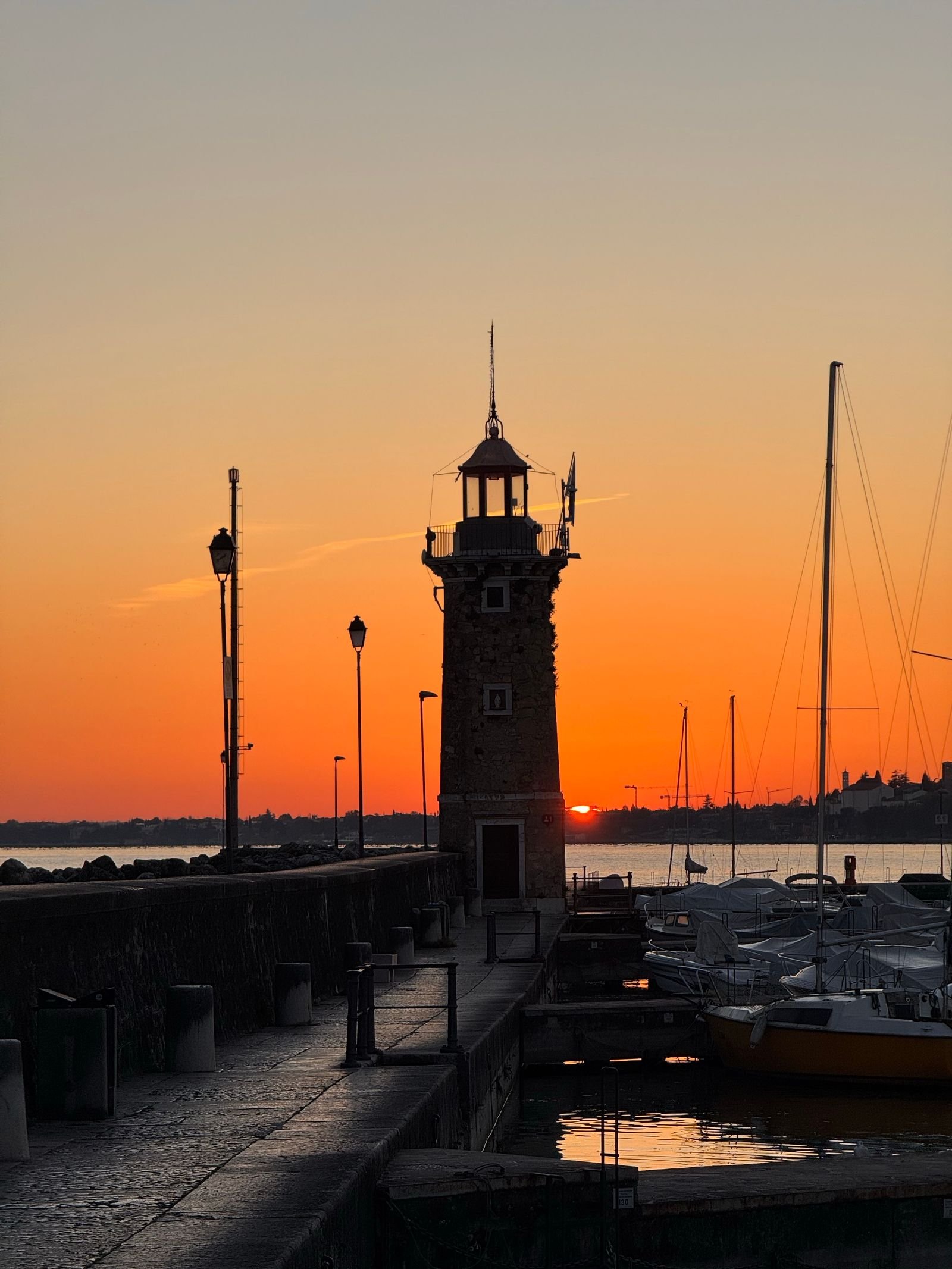 Il faro del porto di Desenzano del Garda al tramonto — punto di partenza dei pazienti di Impianti Dentali Tirana